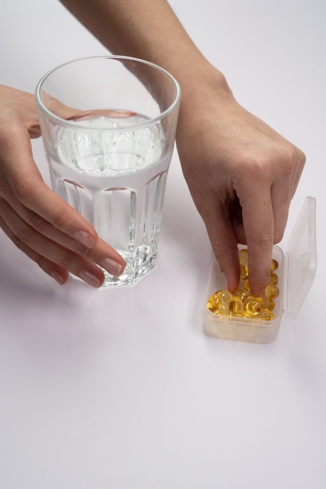 Hand selecting supplements from a pill box beside a glass of water - does vitamin B12 give you energy